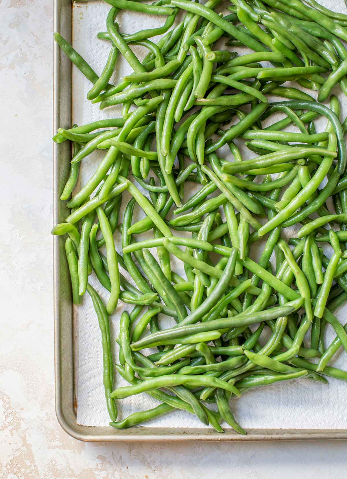 Photo of fresh green beans spread out on a paper towel-lined baking sheet.