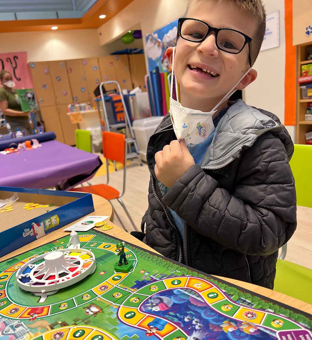 Little boy smiling at camera, standing over a board game.