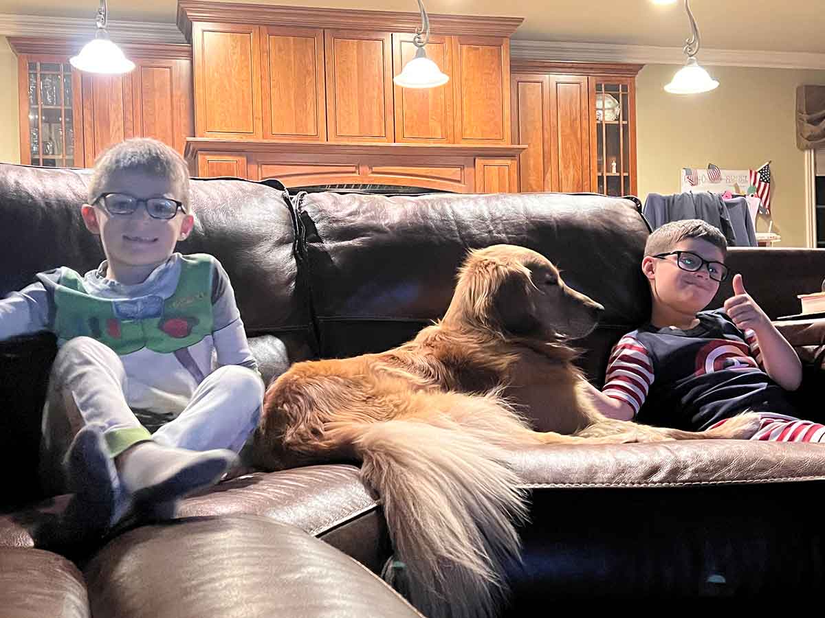 Golden Retriever dog laying in between two boys on a couch.