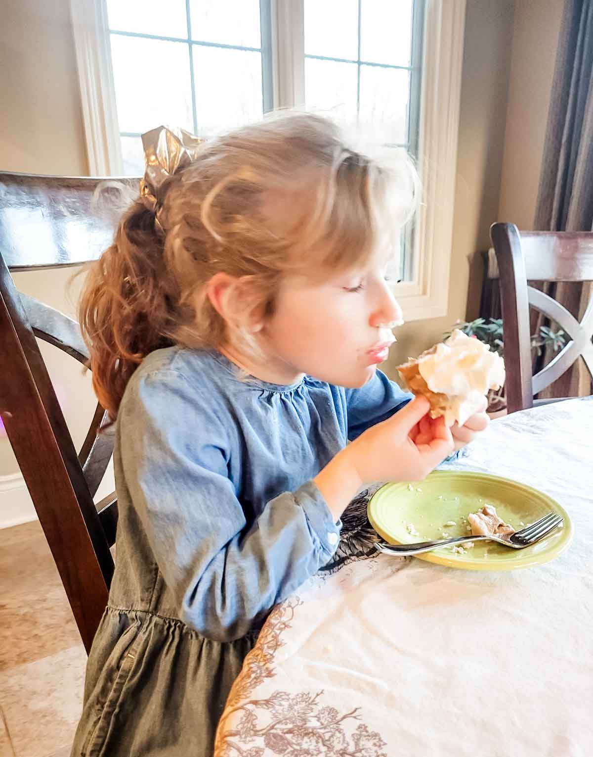 Little girl with her eyes closed taking a bite out of a piece of pumpkin pie.