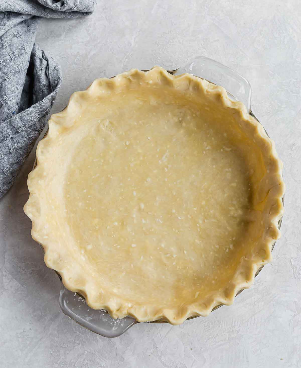 A glass pie plate with pie dough shaped and fluted inside of it.