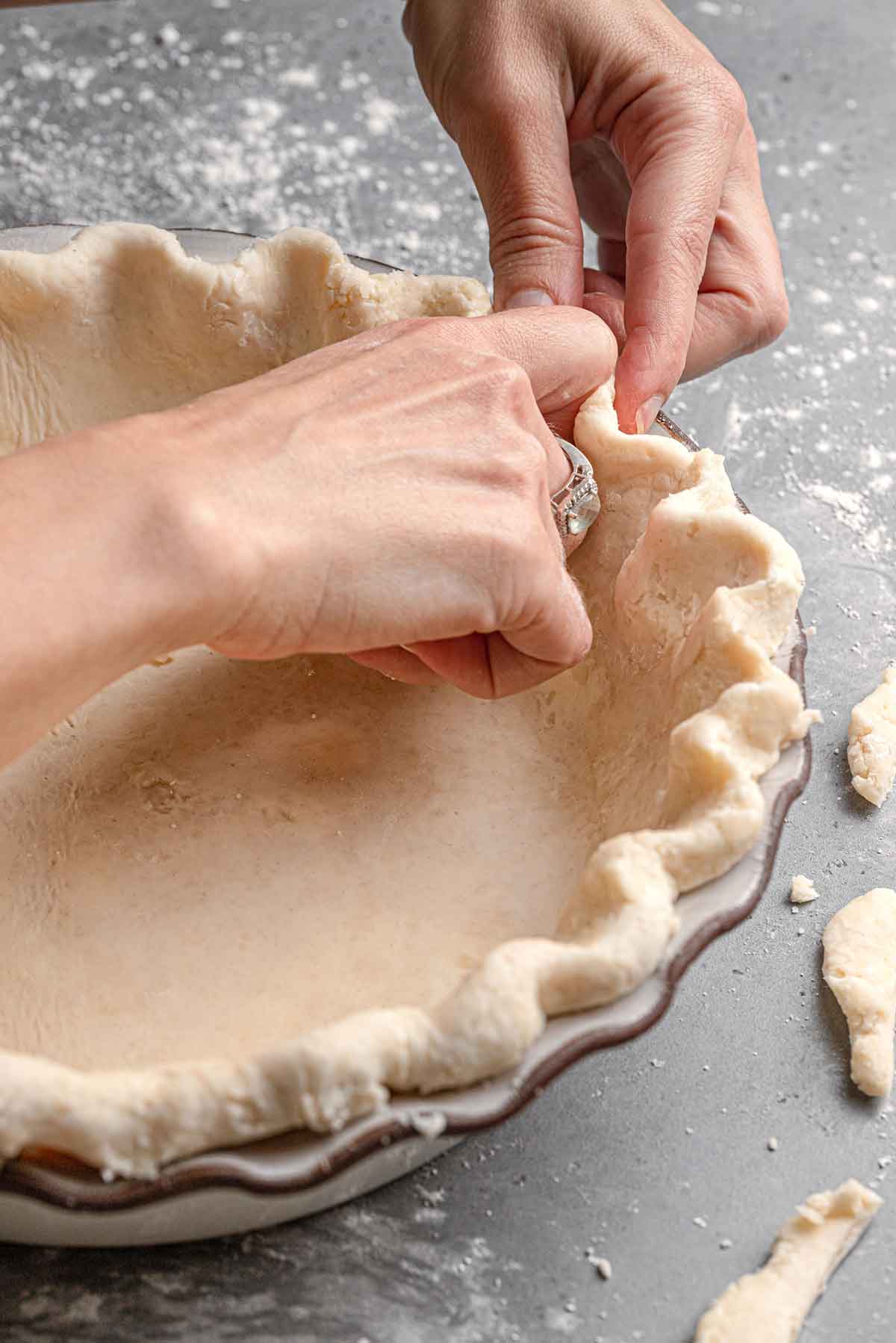 Photo of two hands making the crimping along the edges of a pie crust.