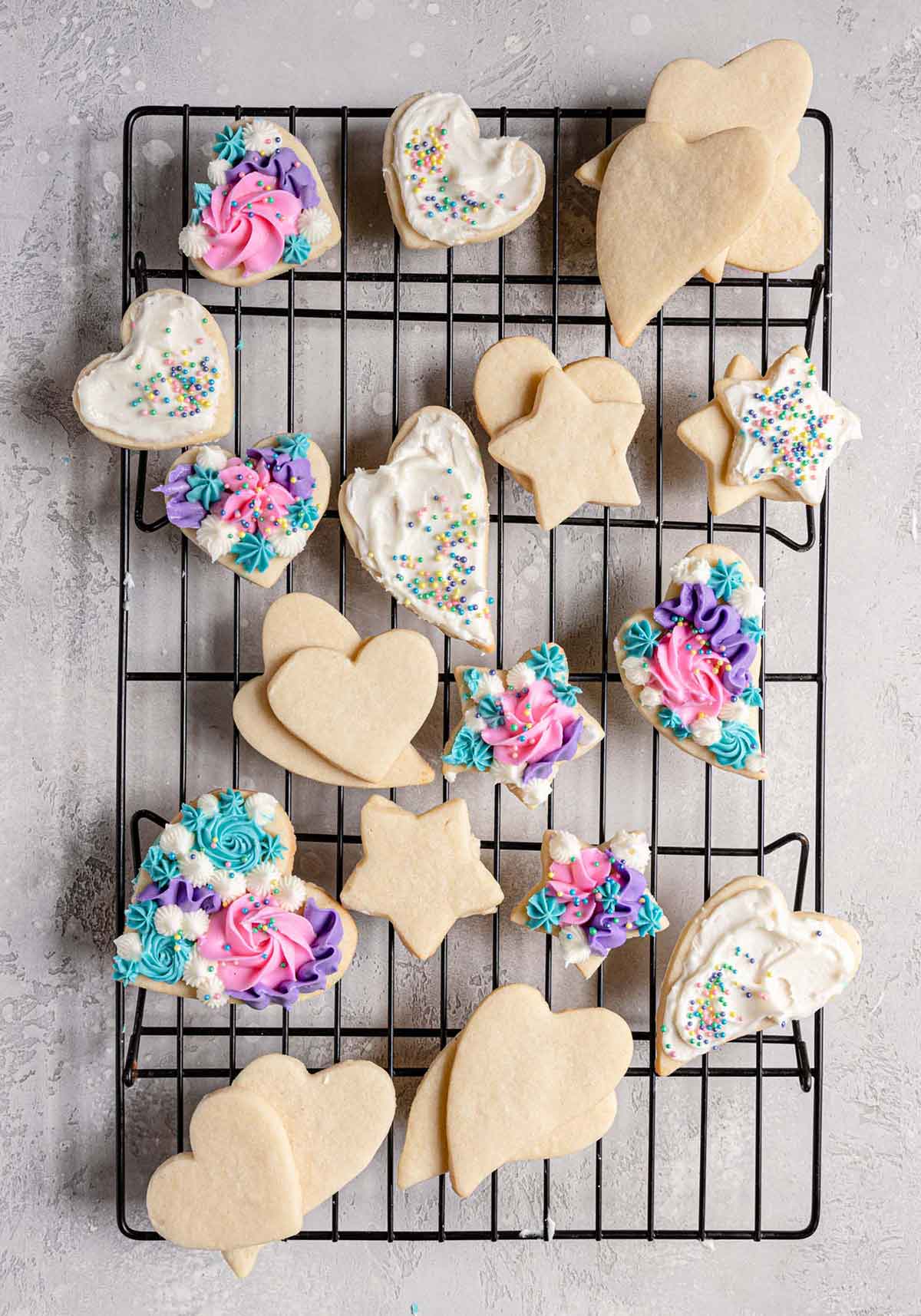 Cut out sugar cookies, some decorated and some not, on a wire cooling rack.