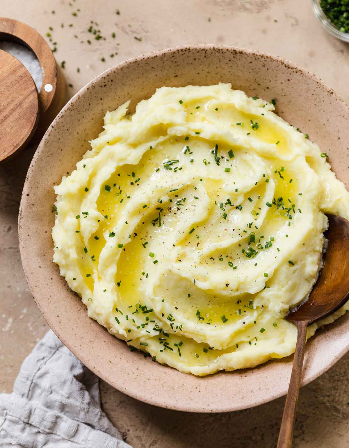 Overhead photo of pink rustic bowl full of mashed potatoes sprinkled with chopped chives and a wooden spoon nestled inside.