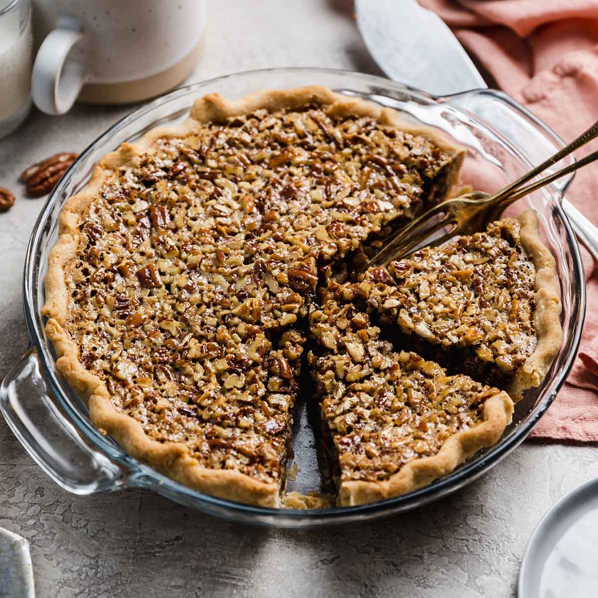 Pecan pie in glass pie dish with two slices cut away and fork in dish.