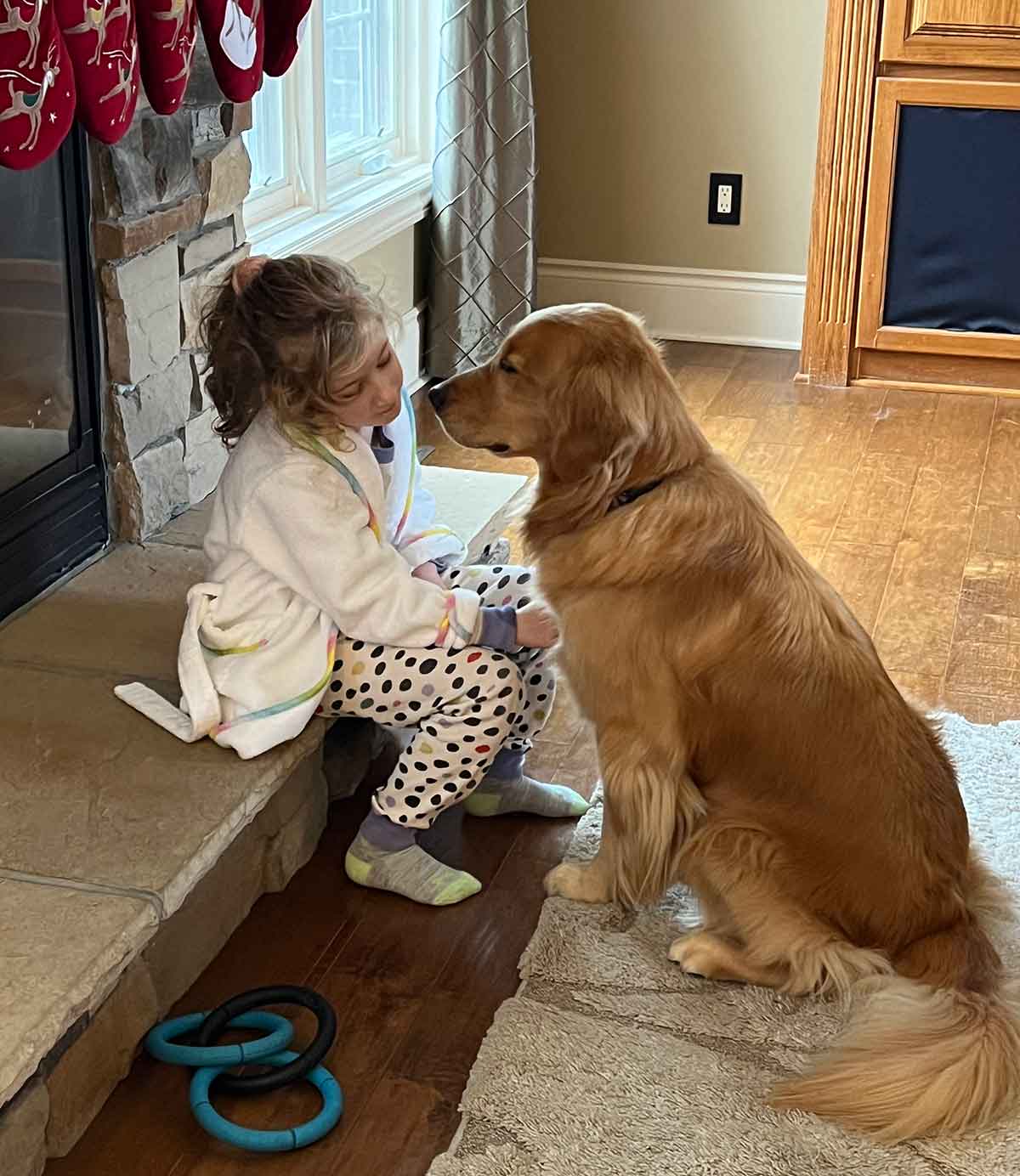Girl sitting on fireplace hearth with Golden Retriever dog sitting in front of her facing her.