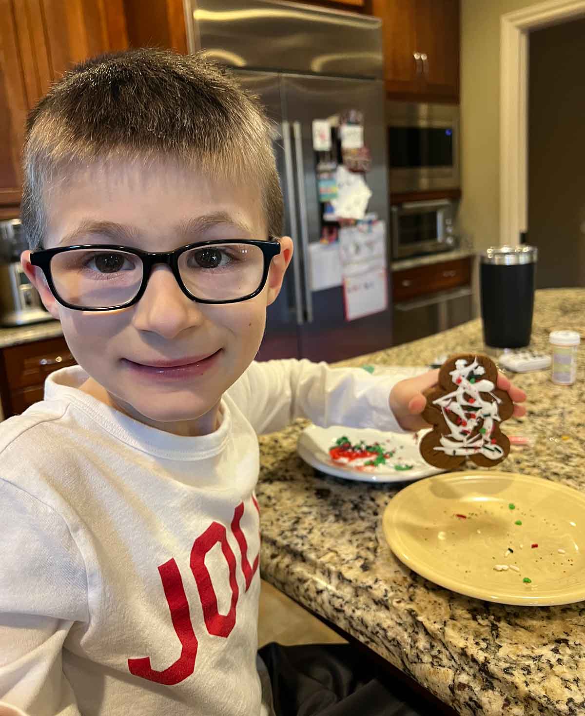 Little boy sitting at a counter holding a decorated gingerbread man cookie.