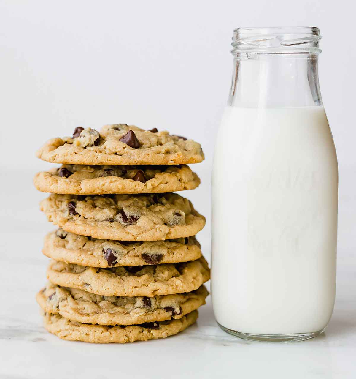 A stack of peanut butter oatmeal chocolate chip cookies next to a glass jar of milk.