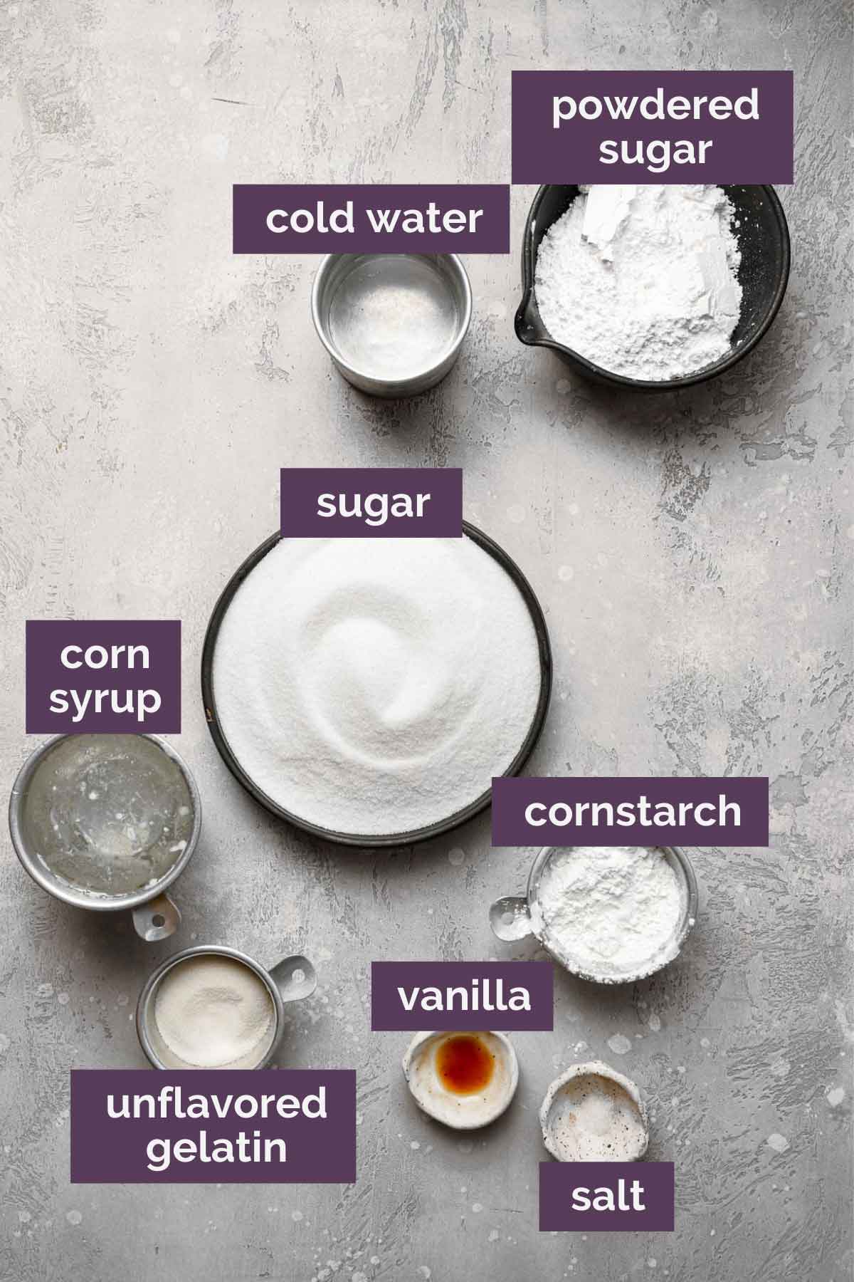 Ingredients for homemade marshmallows prepped and labeled: powdered sugar, cold water, sugar, corn syrup, cornstarch, vanilla, unflavored gelatin, and salt.