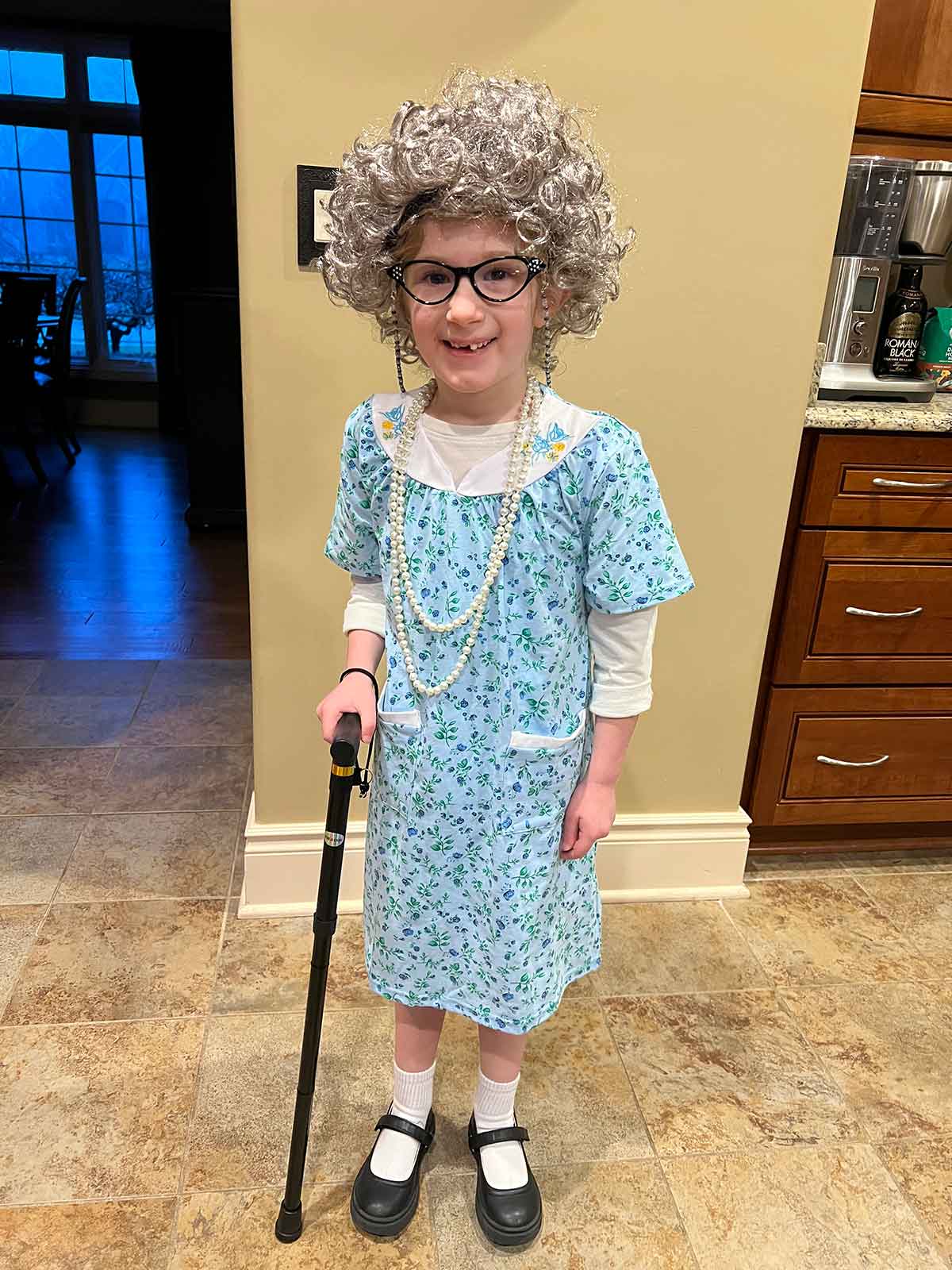 Little girl dressed in an old lady costume and holding a cane.