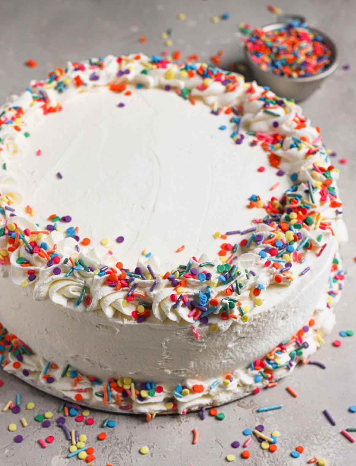 Assembled homemade ice cream cake frosted in whipped cream and decorated with rainbow sprinkles.