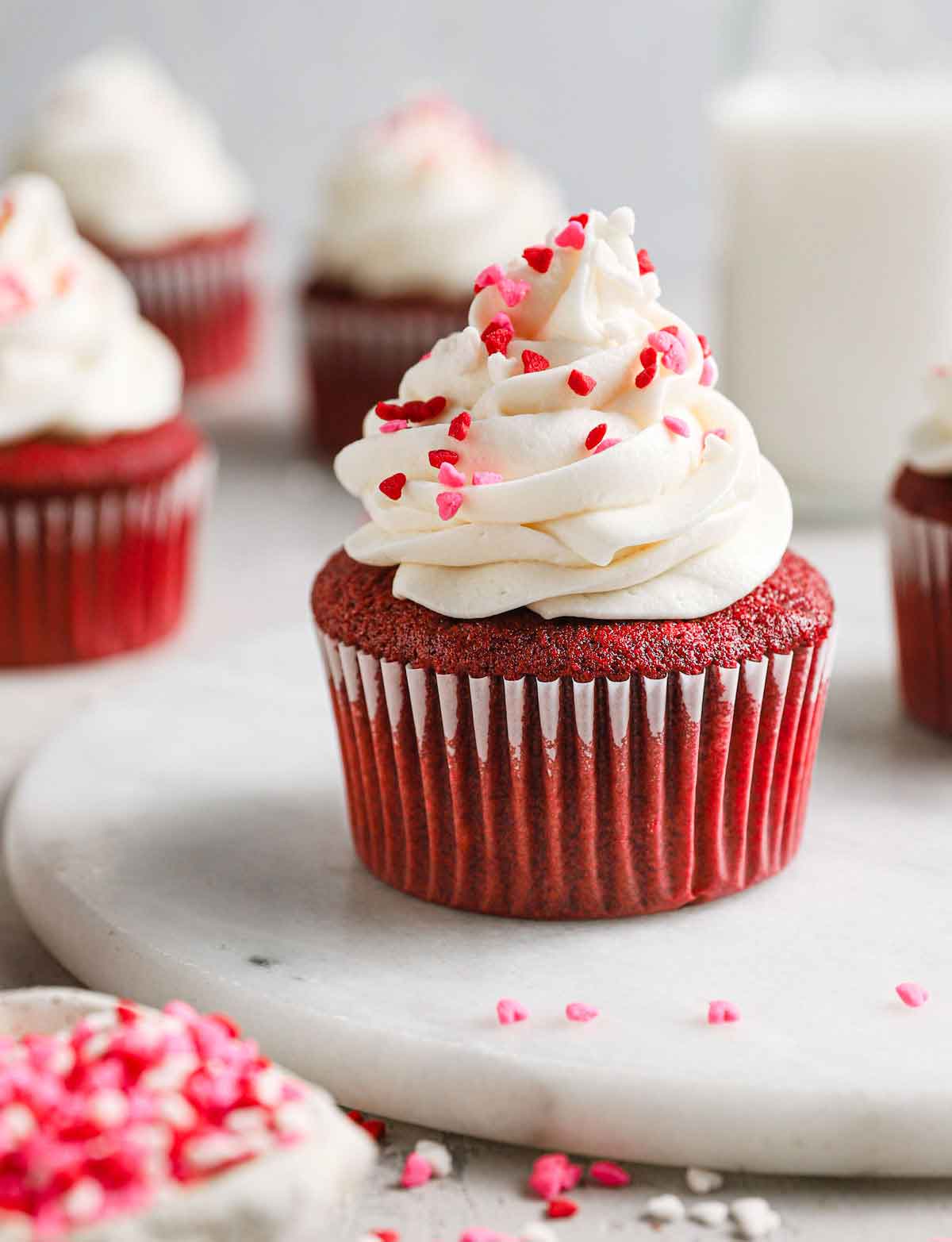 Red velvet cupcake with cream cheese frosting and red and pink heart sprinkles.