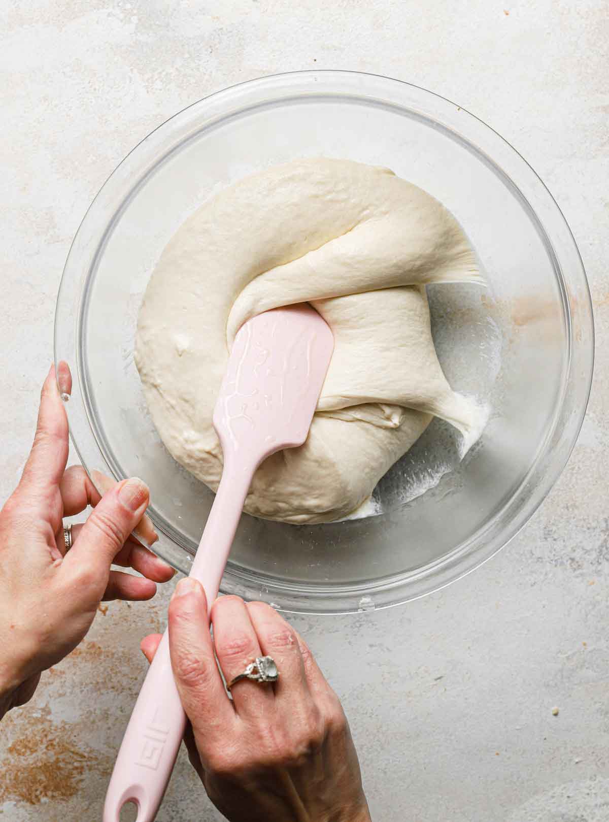 A rubber spatula being used to fold ciabatta dough over itself in a glass bowl.