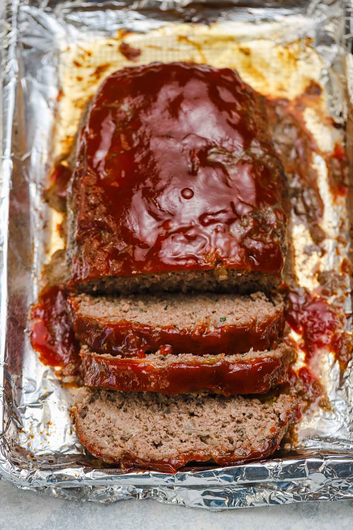 Meatloaf sliced with glaze on top on a foil-lined baking sheet.