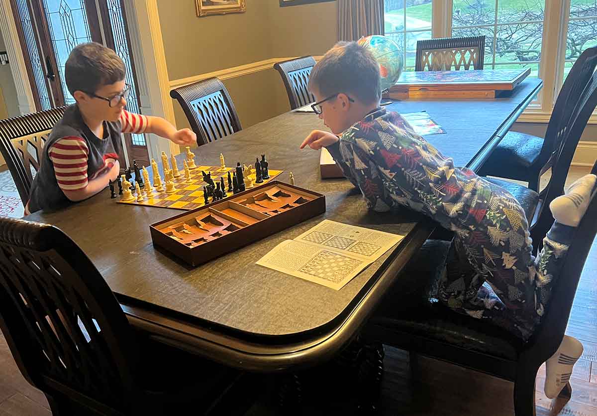 Two boys in pajamas playing chess at a dining room table.
