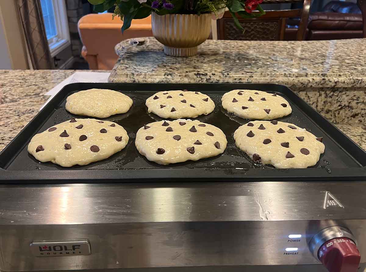 Chocolate chip pancakes cooking on a griddle.