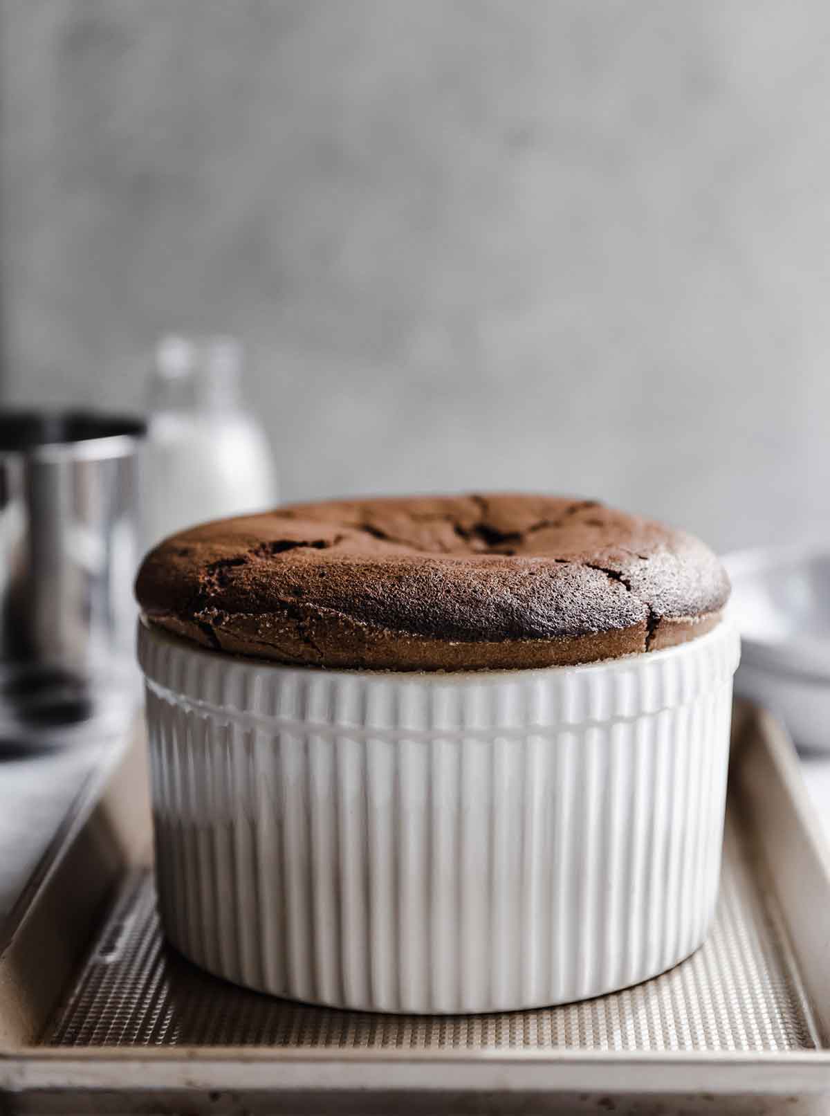 A chocolate souffle in a white porcelain souffle dish set on a baking sheet.