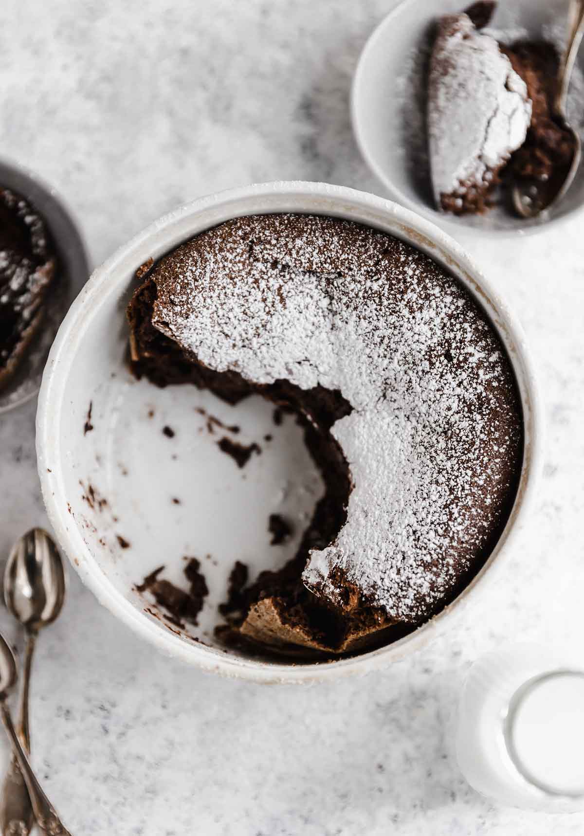 Overhead photo of chocolate souffle with powdered sugar in a souffle dish, with half scooped out.