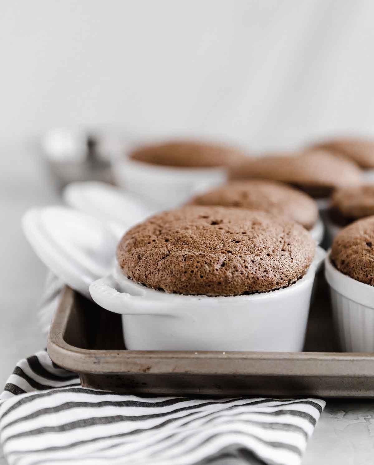 Individual chocolate souffles in small white ramekins sitting on a baking sheet.