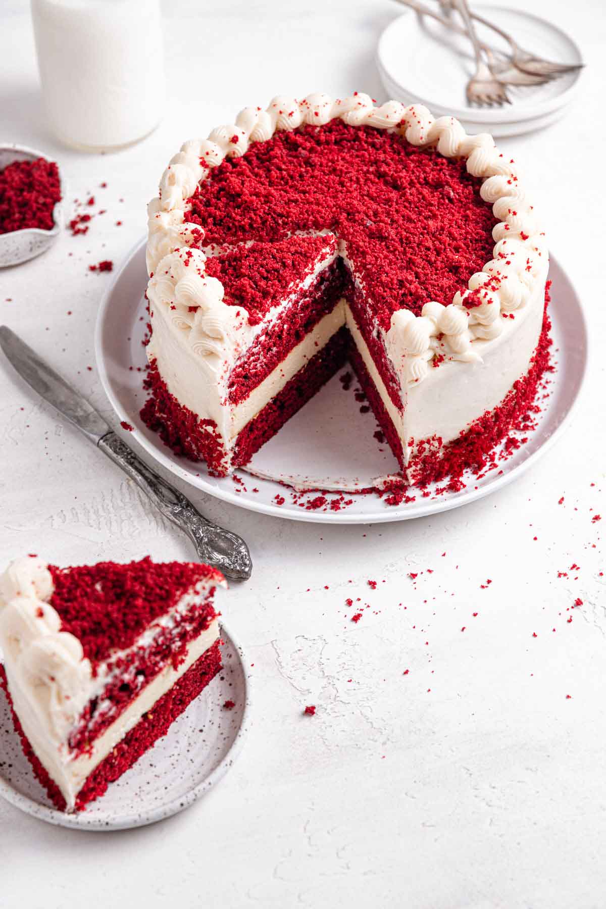 Assembled and decorated red velvet cheesecake on a serving platter with a single slice on a plate to the side.