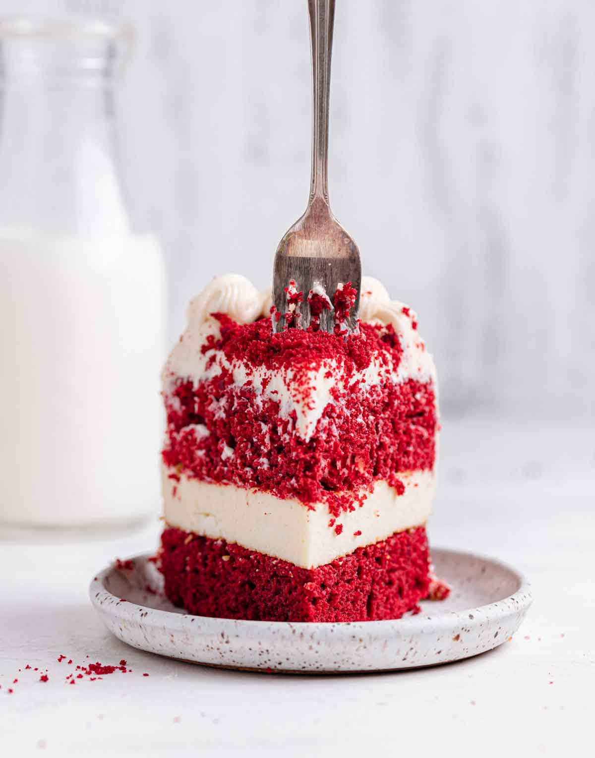 Head-on shot of a slice of red velvet cheesecake with a fork coming down into it from above.