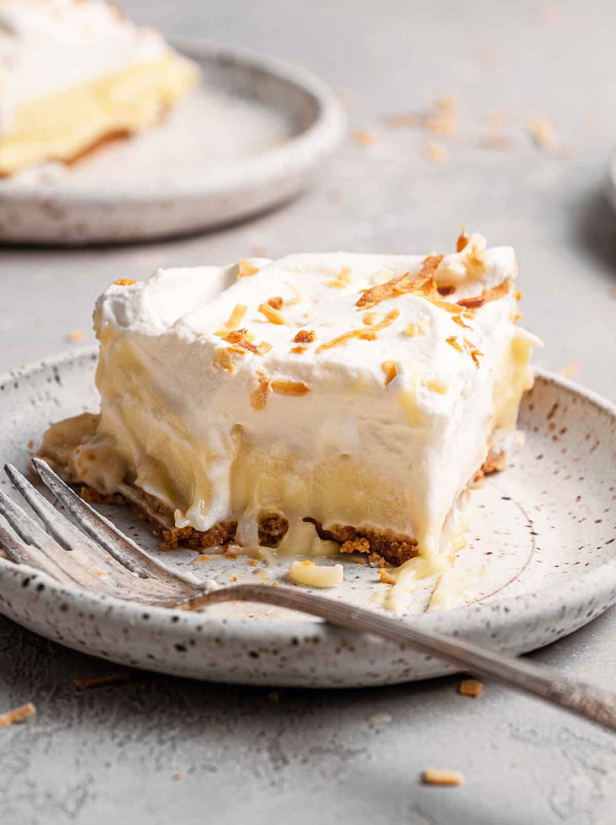 Slice of coconut cream pie on a speckled plate with a fork.