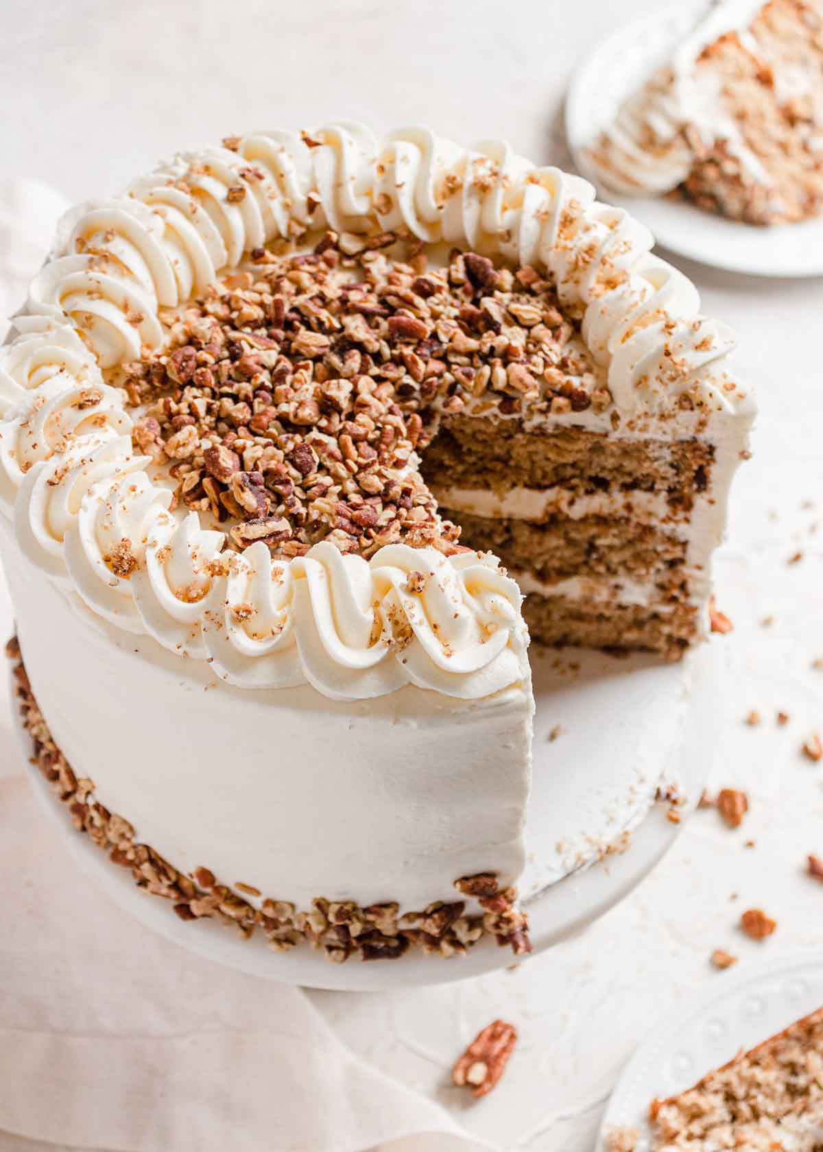 Overhead photo of hummingbird cake with two slices removed, with frosting piped around the edge and chopped pecans in the center.