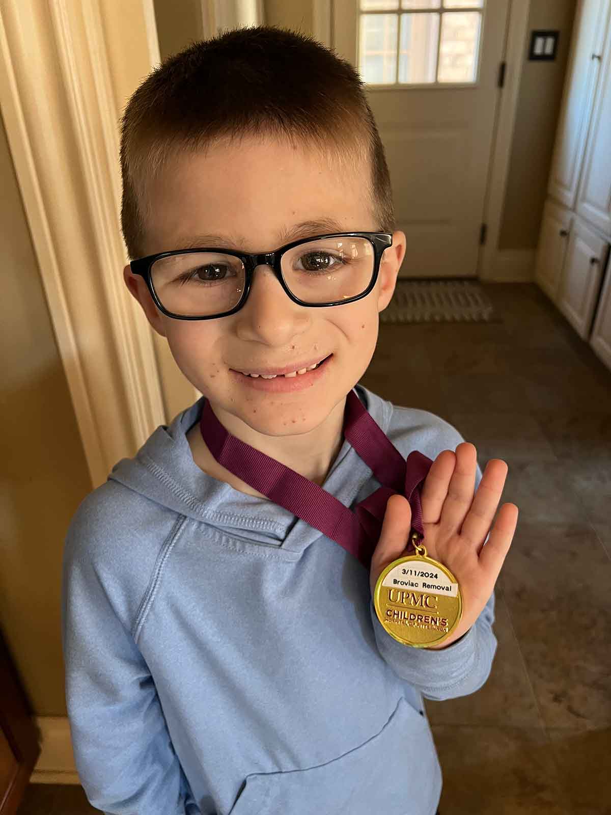 Boy in a light blue hoodie holding a gold medal. 