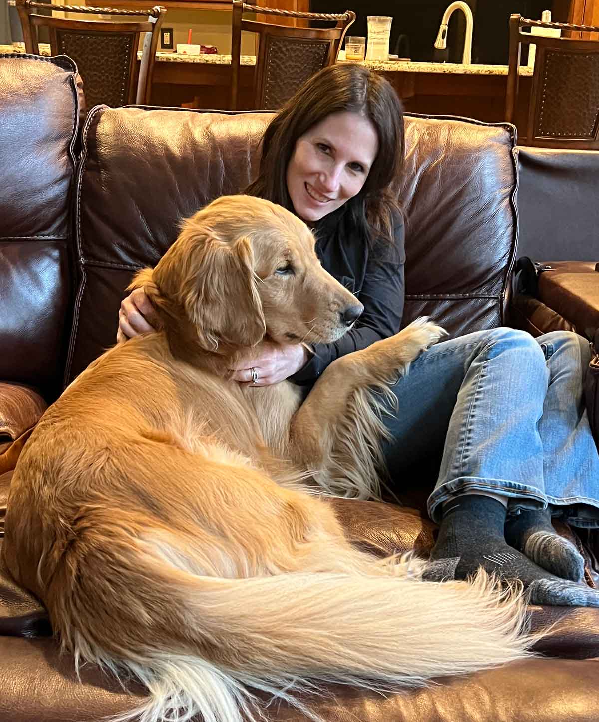 Woman snuggling with a golden retriever on a reclining couch.