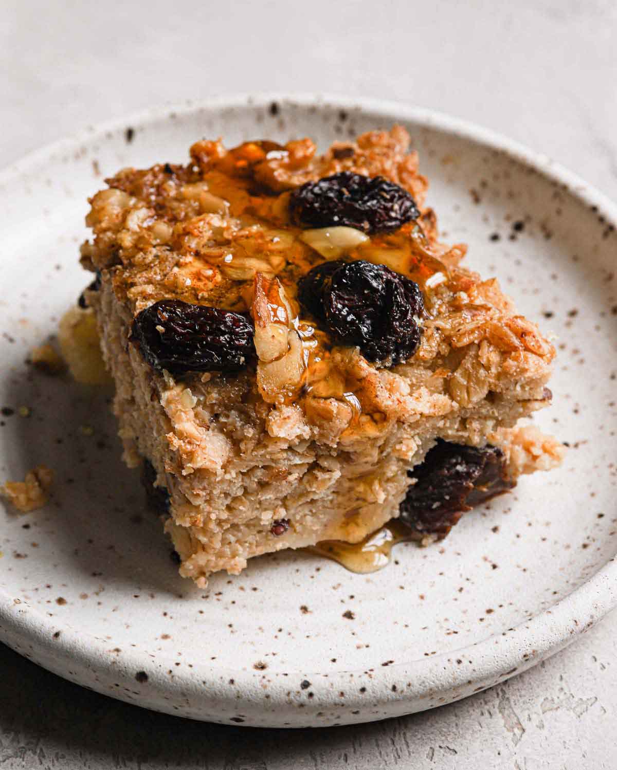 Slice of baked oatmeal with a drizzle of maple syrup on top on a speckled plate.