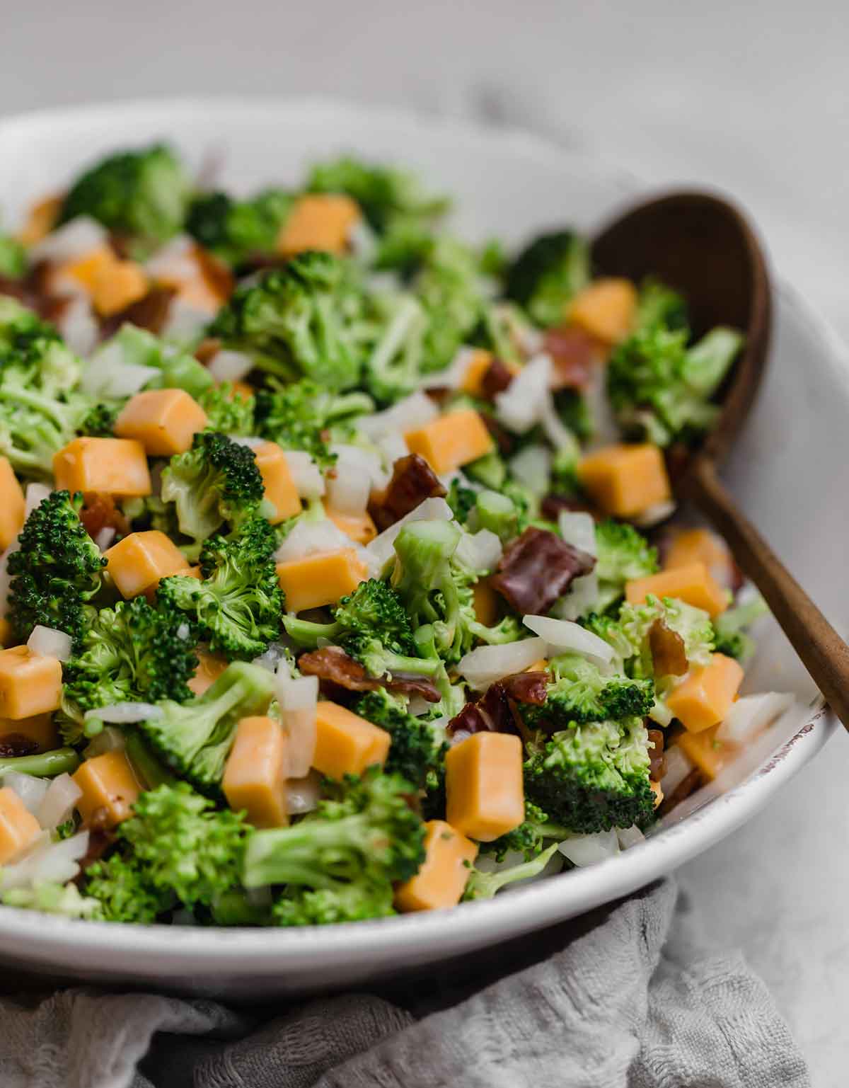 Close up photo of broccoli salad in a white bowl with a wooden serving spoon.