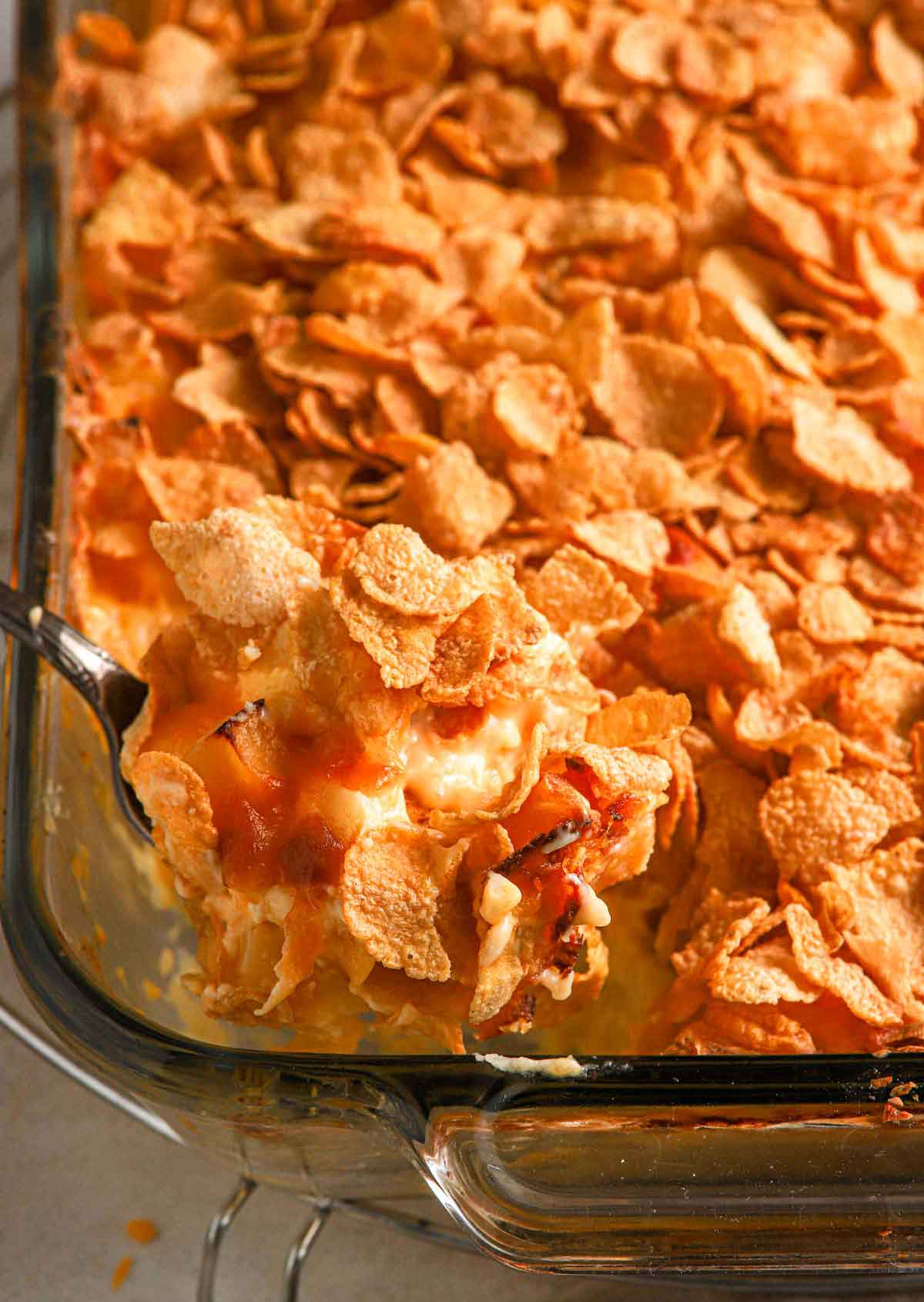 Serving spoon scooping out cheesy potato casserole from a baking dish.