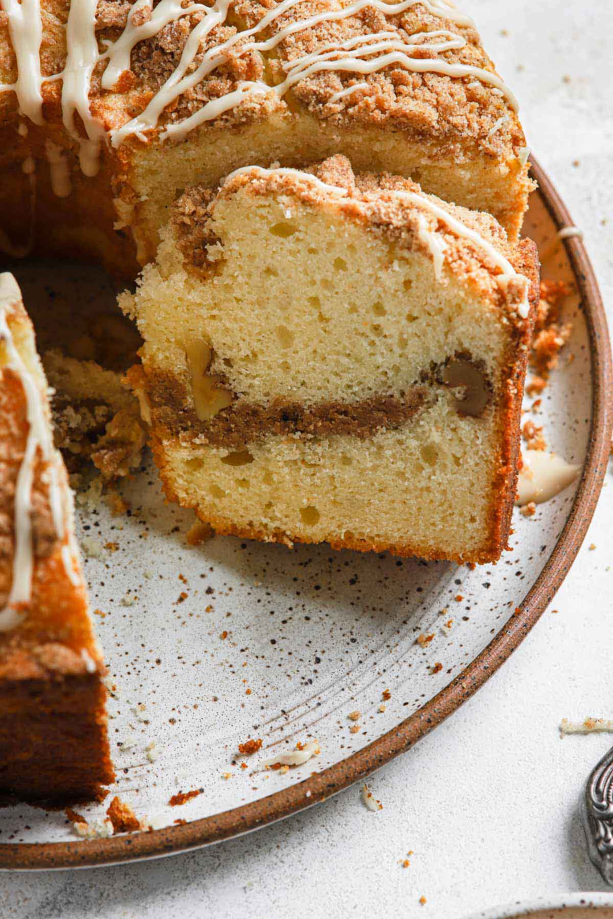 Close up photo of slice of sour cream coffee cake leaning up against the remainder of the uncut cake.