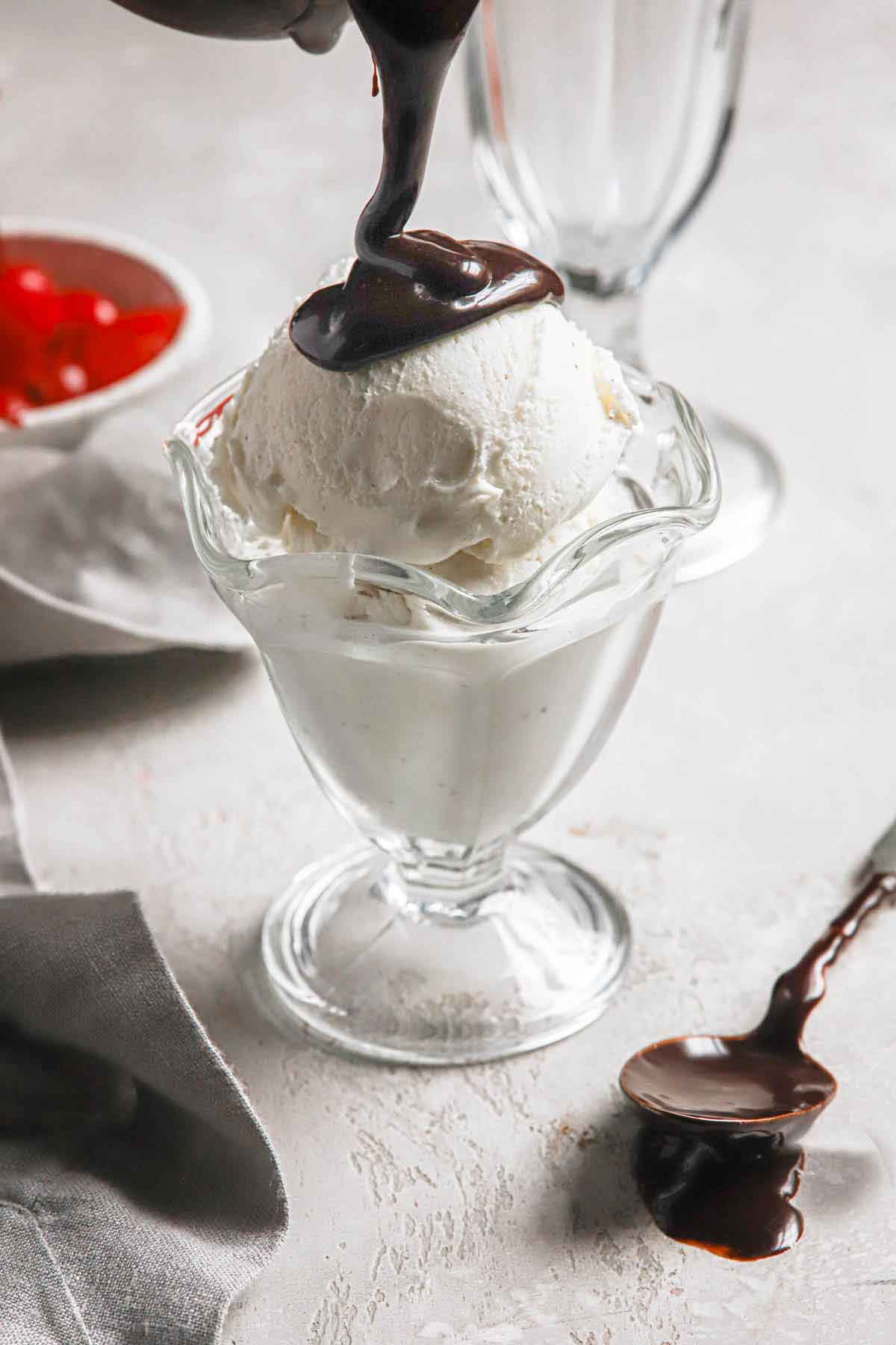 Vanilla ice cream in a parfait glass hot fudge being poured on top.