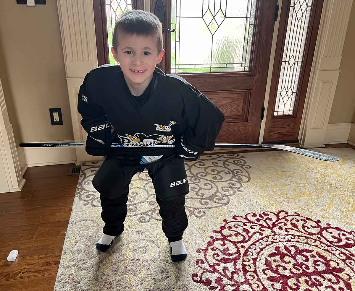 Little boy with hockey equipment on bend over holding hockey stick over his knees.