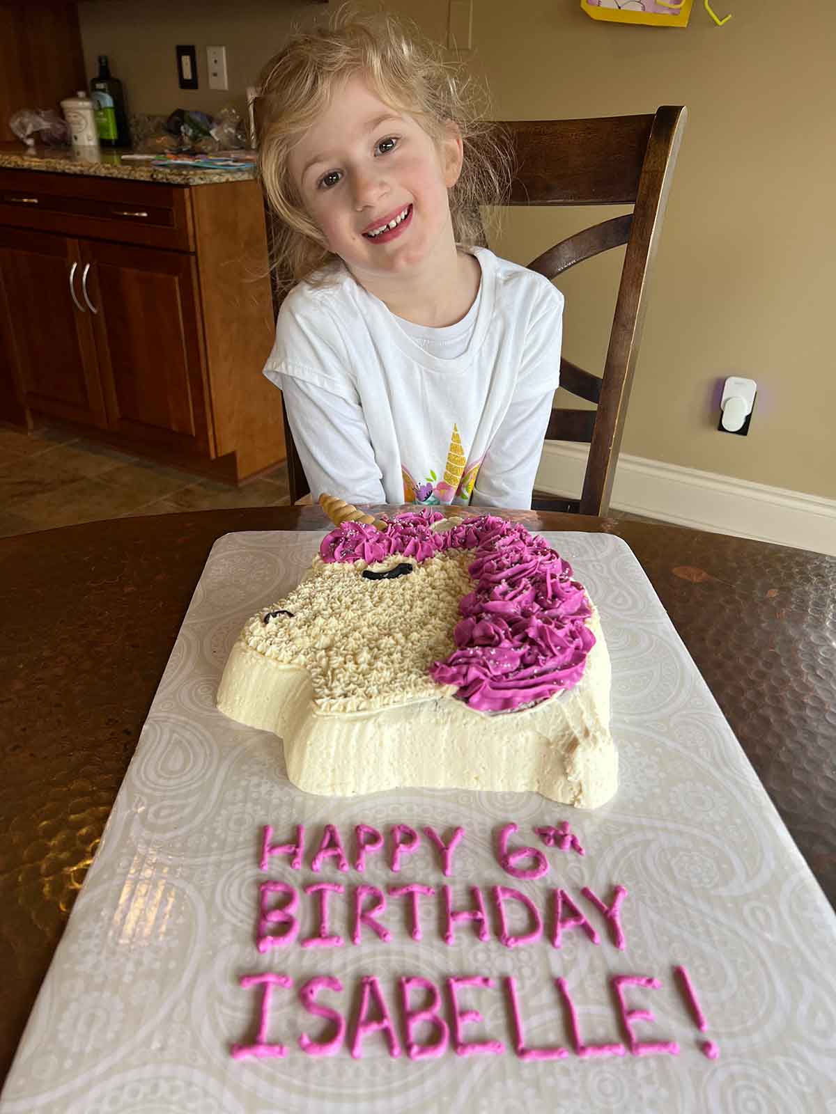 Little girl sitting in front of a unicorn cake with the words Happy 6th Birthday Isabelle.