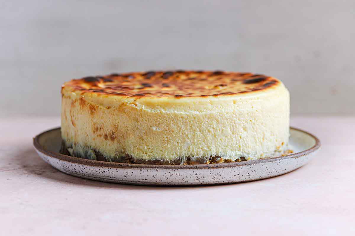 Straight on view of New York cheesecake on serving platter with browned top.