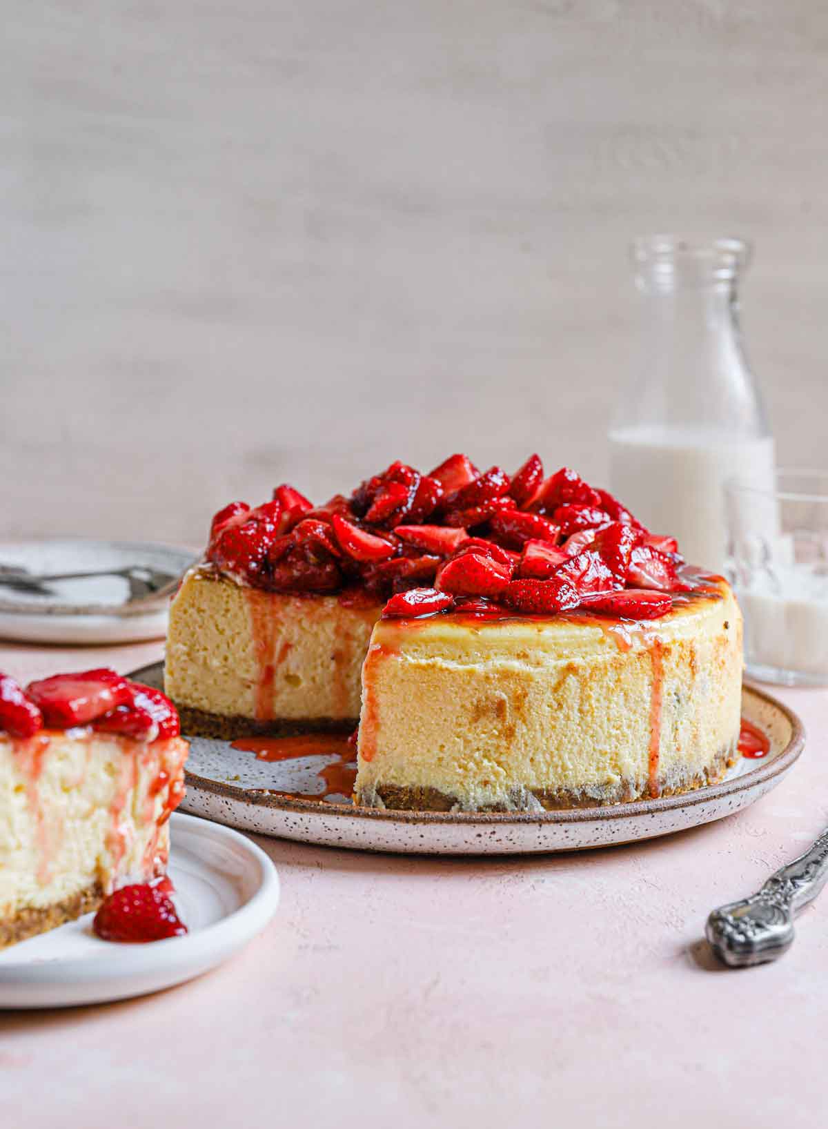 Side view of New York cheesecake with strawberries on top and one slice removed.