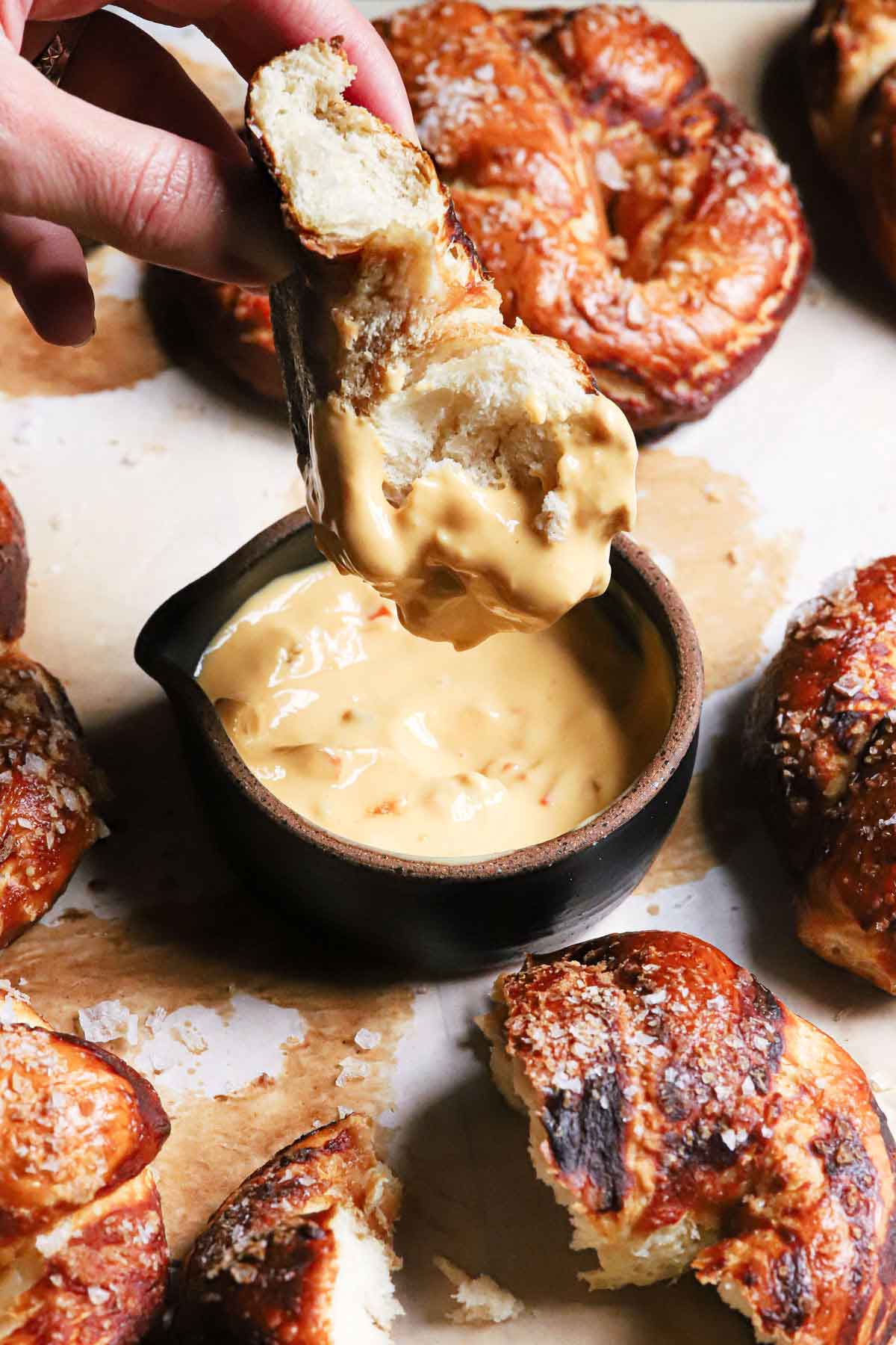 A soft pretzel being dipped into a small bowl of spicy cheese sauce.