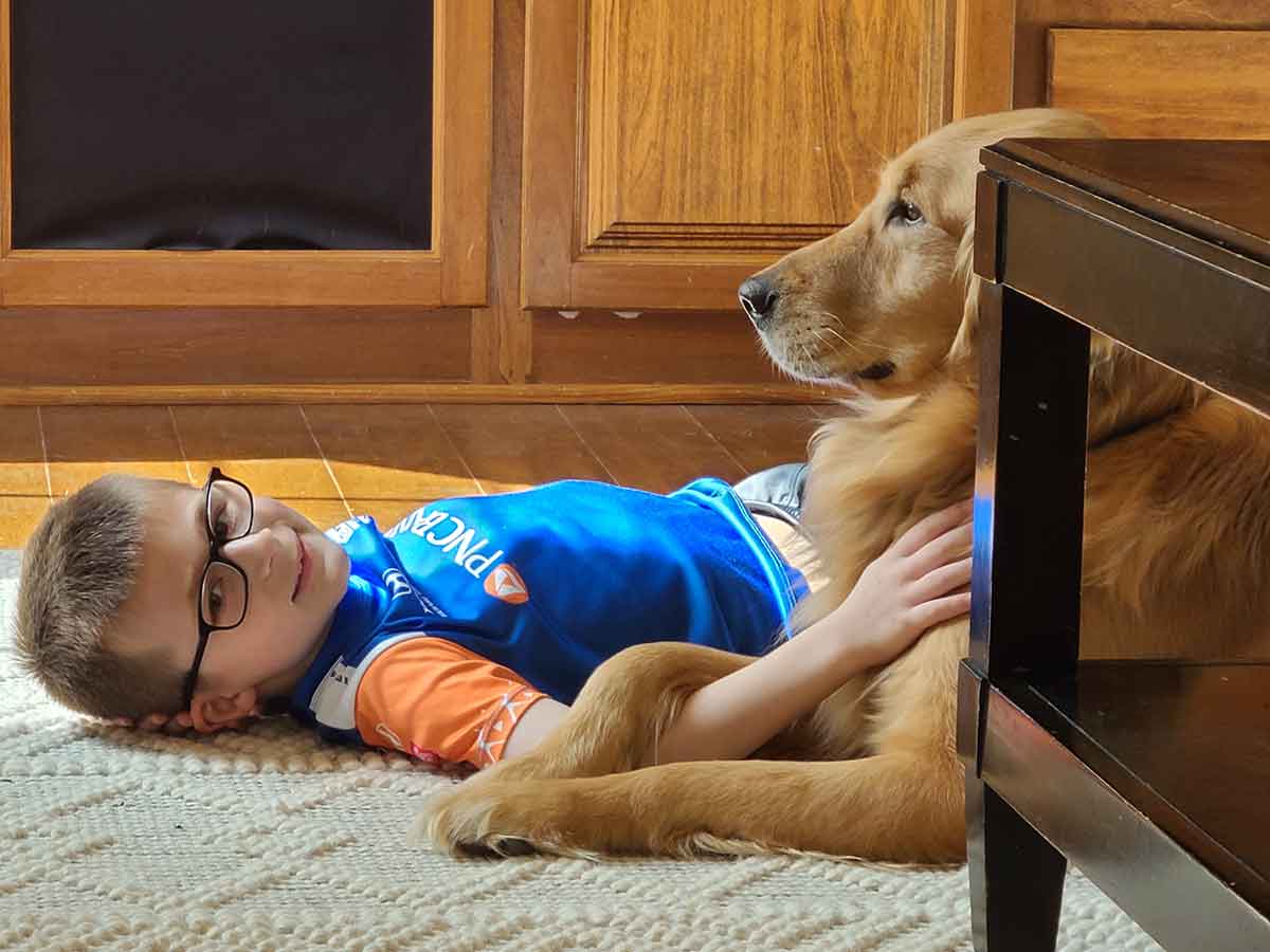 Little boy laying on the floor next to a Golden Retriever.