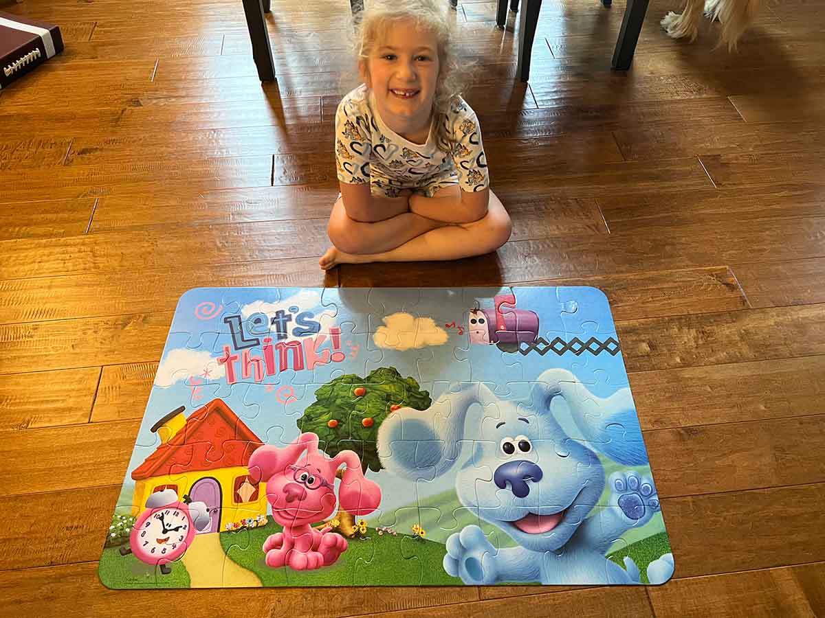 Little girl sitting cross legged in front of a completed floor puzzle, smiling.