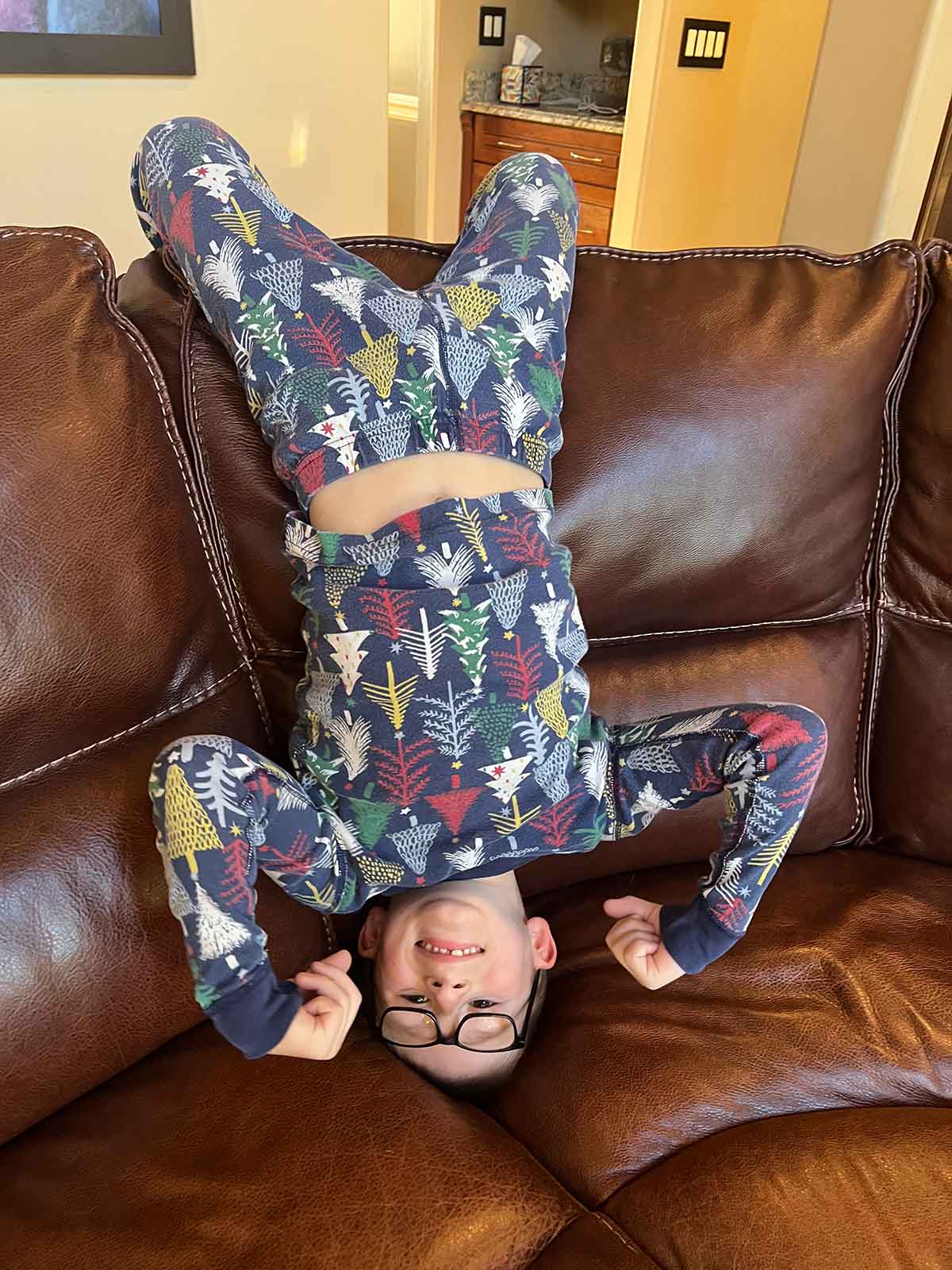 Little boy in winter pajamas standing on his head on a couch.