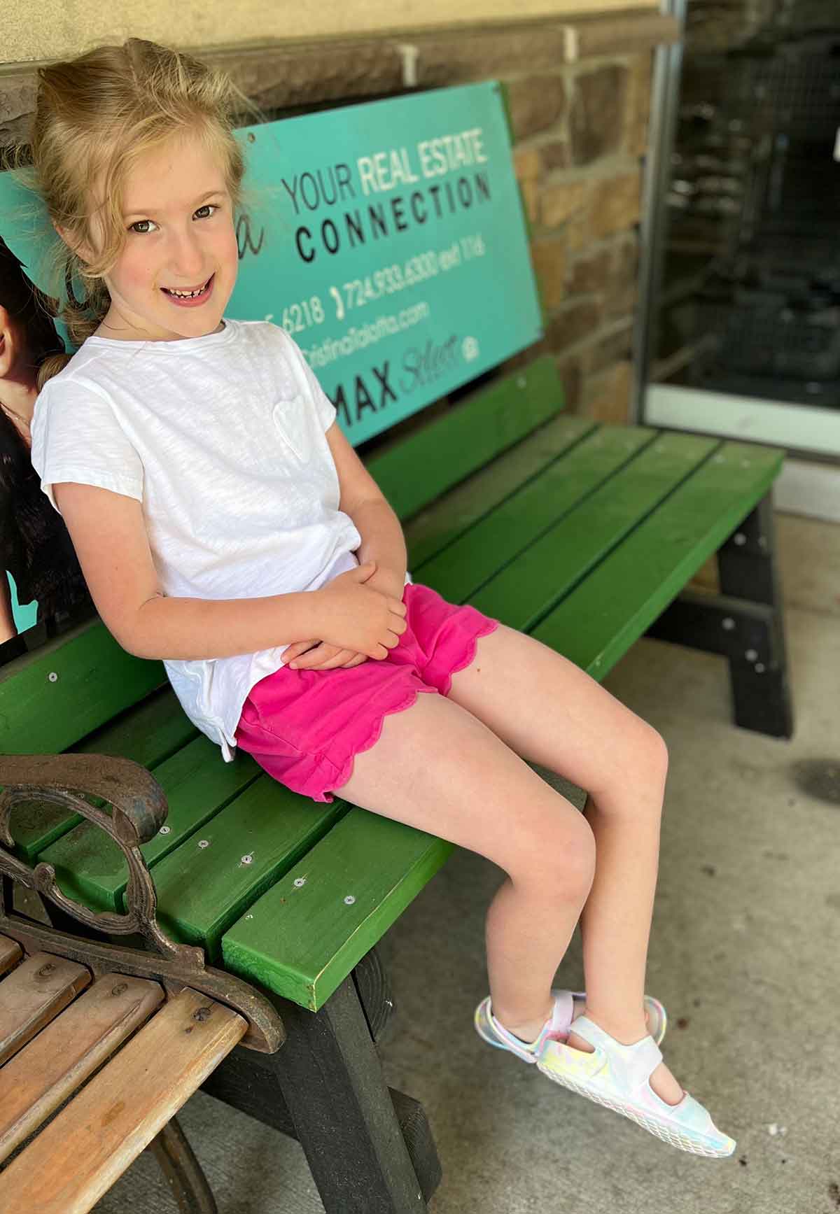 Little girl sitting on a bench in shorts and a tshirt.