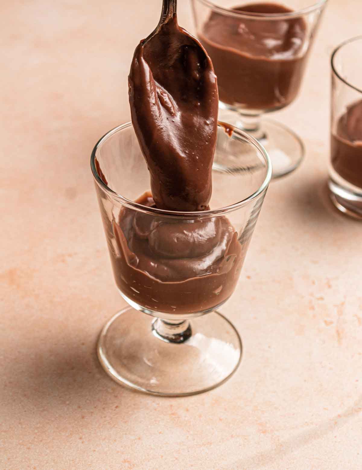 Chocolate pudding being spooned into glass parfait cups.