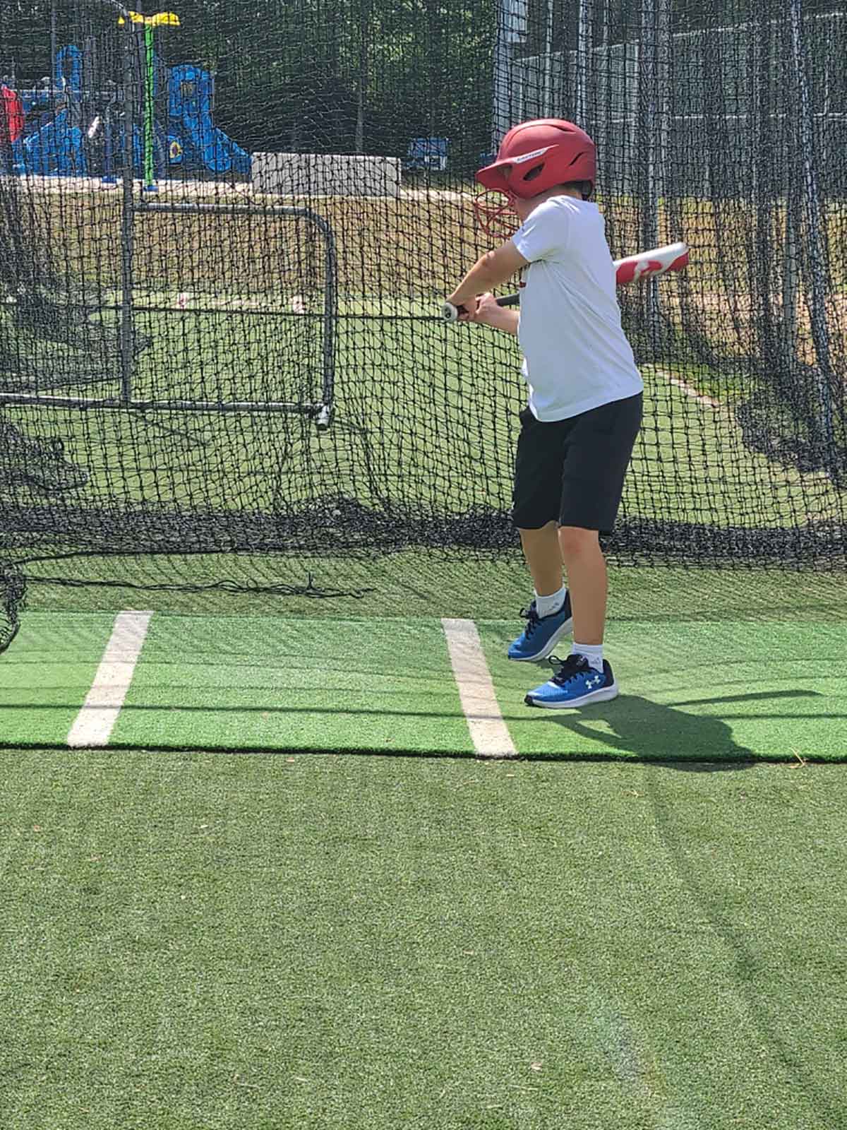 Boy in a red helmet in a baseball batting cage.