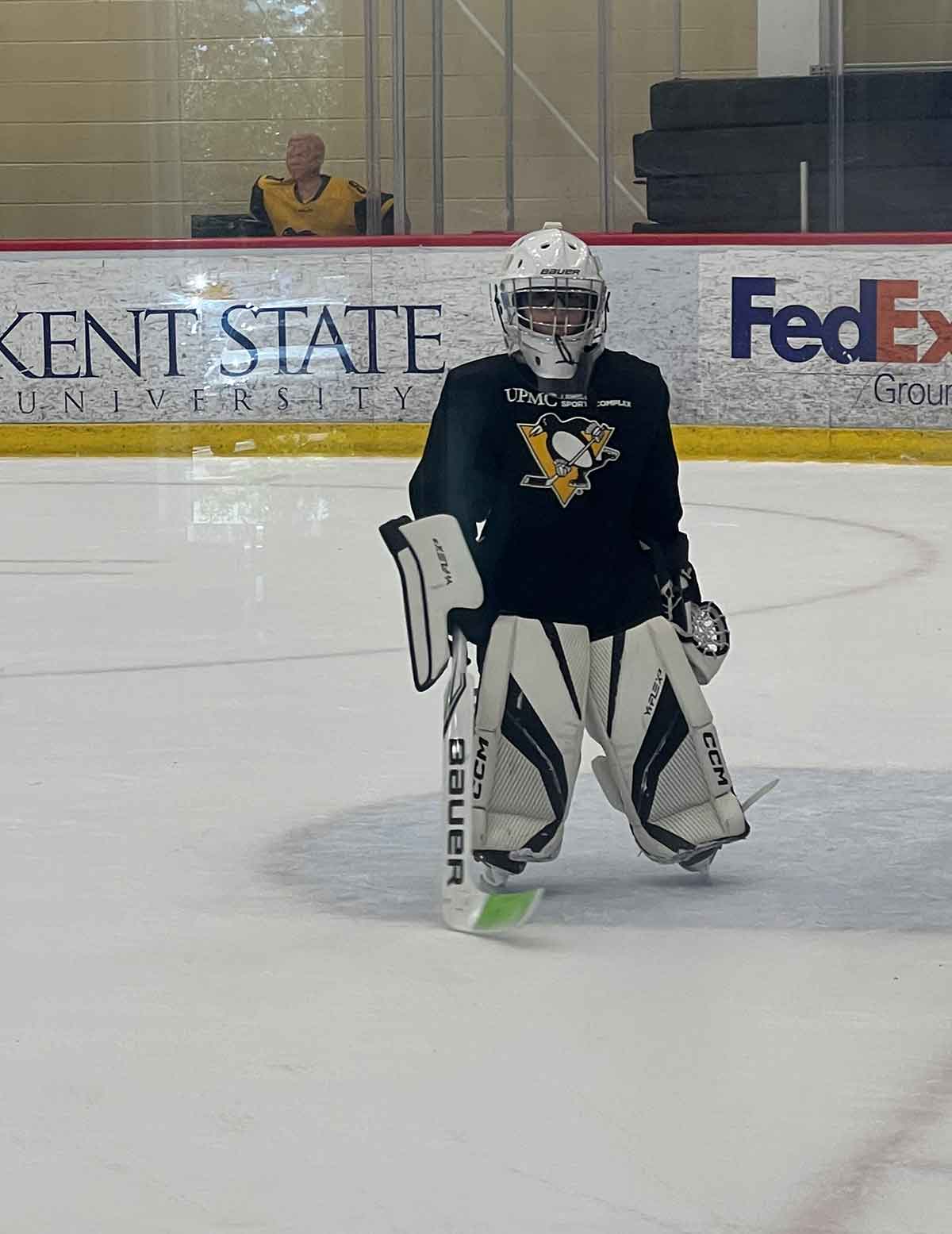 Boy on ice wearing a black jersey, white helmet and goalie equipment.