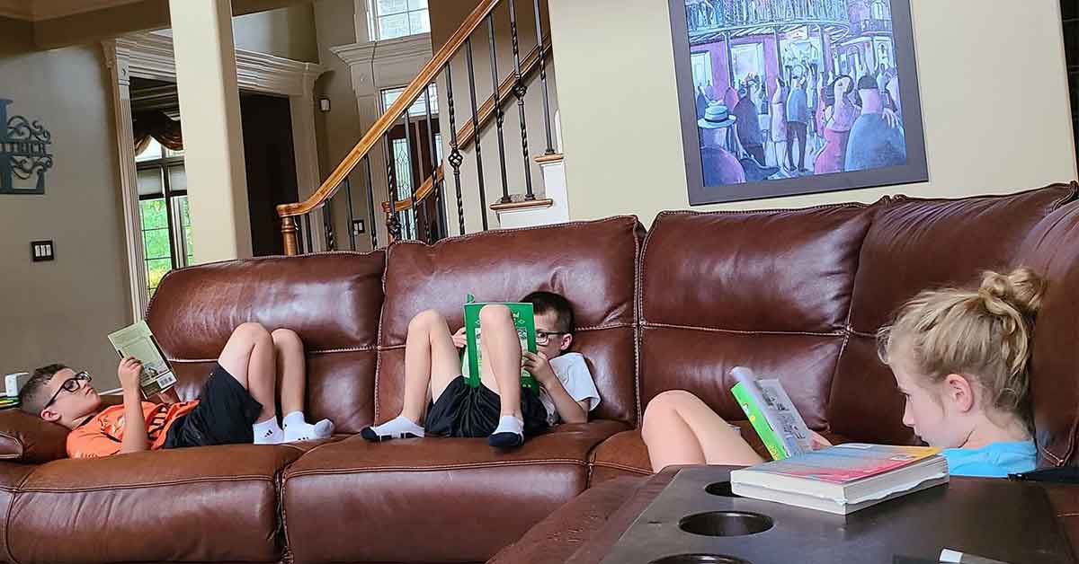 Three kids sitting on a couch reading books.