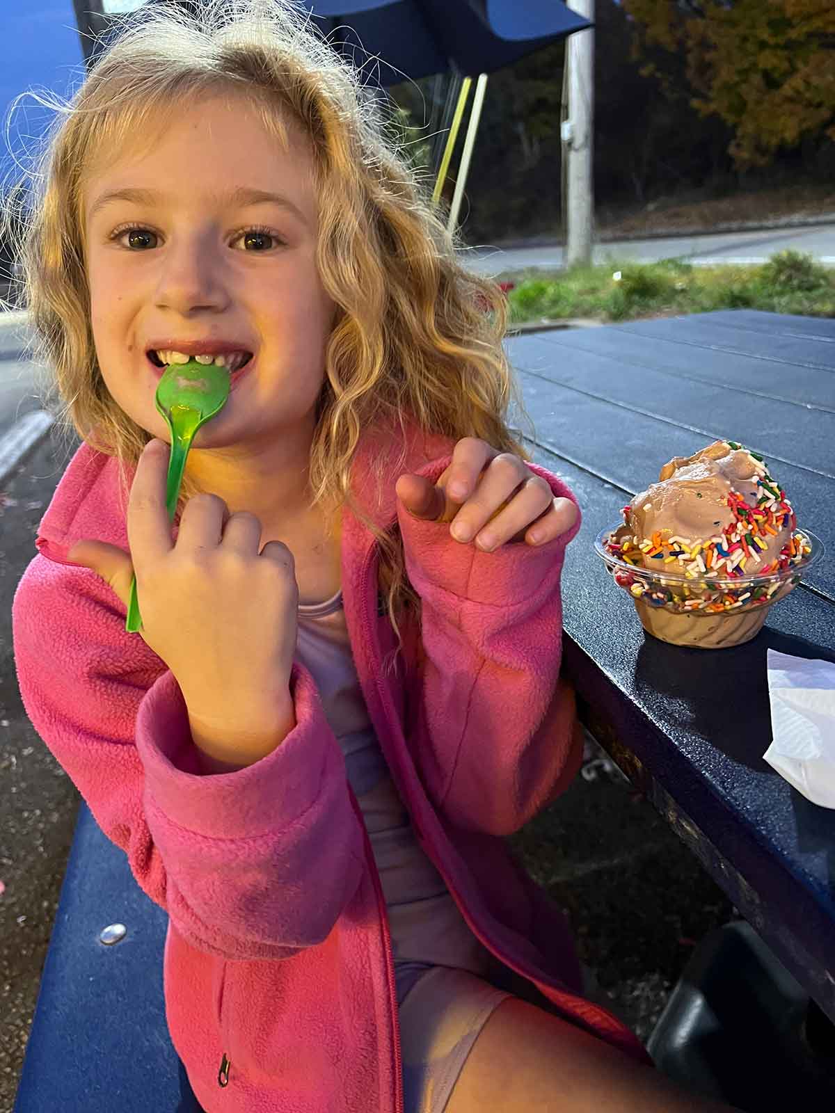 Little girl eating ice cream with sprinkles at a picnic table.