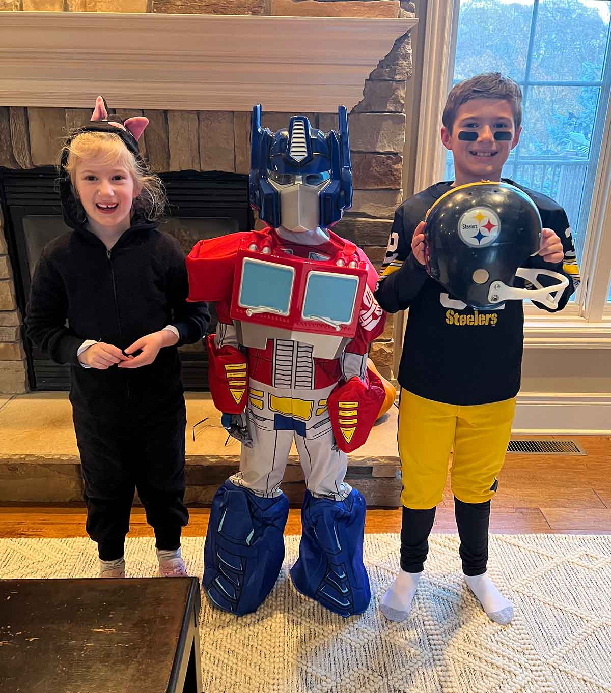 Three kids in Halloween costumes - a black cat, Optimus Prime transformer, and a football player.