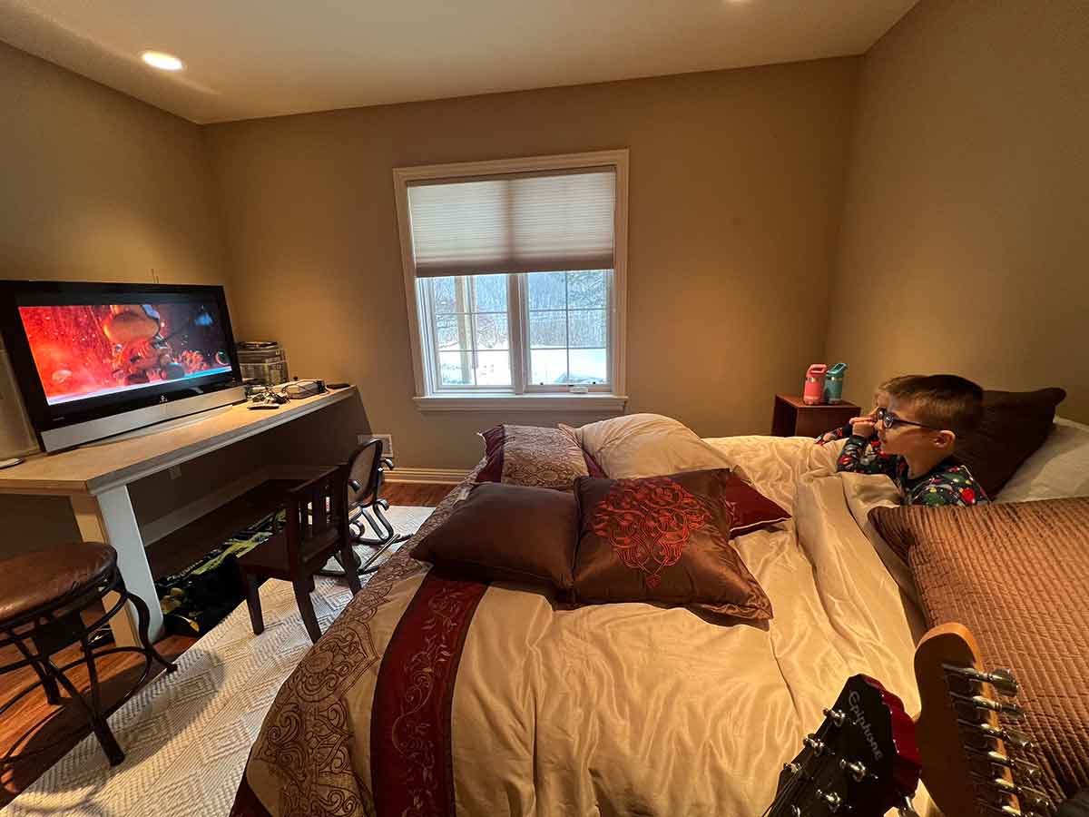 Boy and girl sitting on a bed watching a movie.
